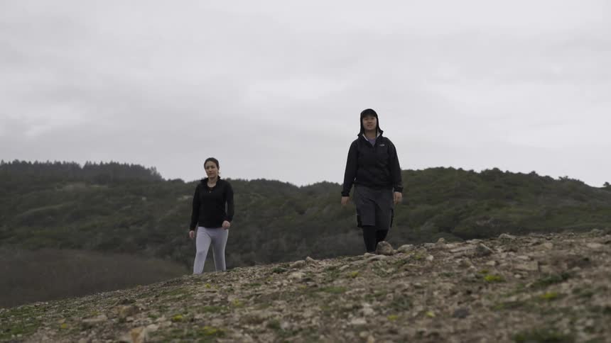 Two people are hiking over a hill on a cloudy day