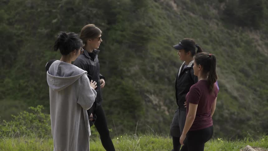 Four women talk in a field overlooking a hill