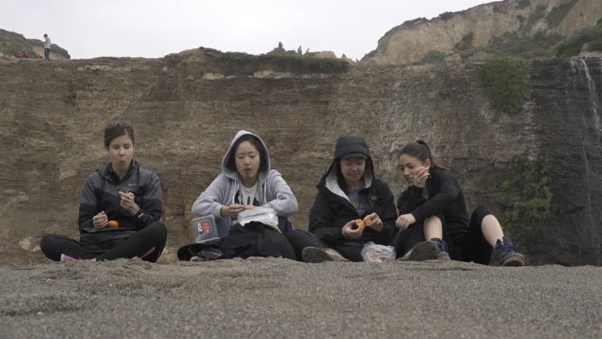 Four women sit and eat a picnic lunch on a mountain on an overcast day