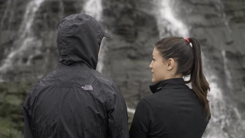 Two people stand near a waterfall in the wilderness