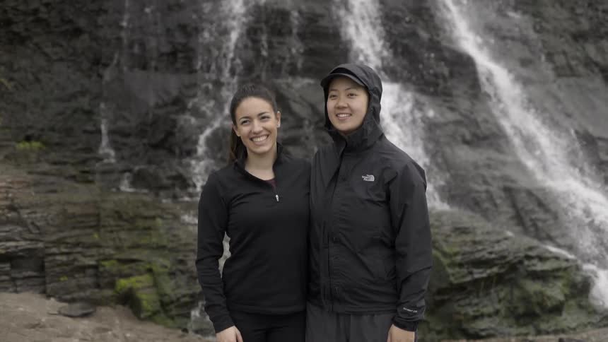 Two smiling women pose before a waterfall