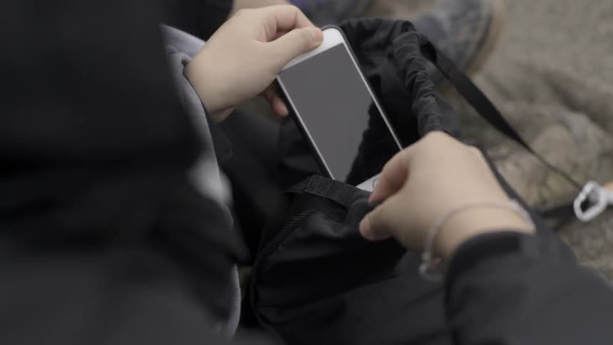 Close up of person placing smartphone into bag in everyday lifestyle moment.