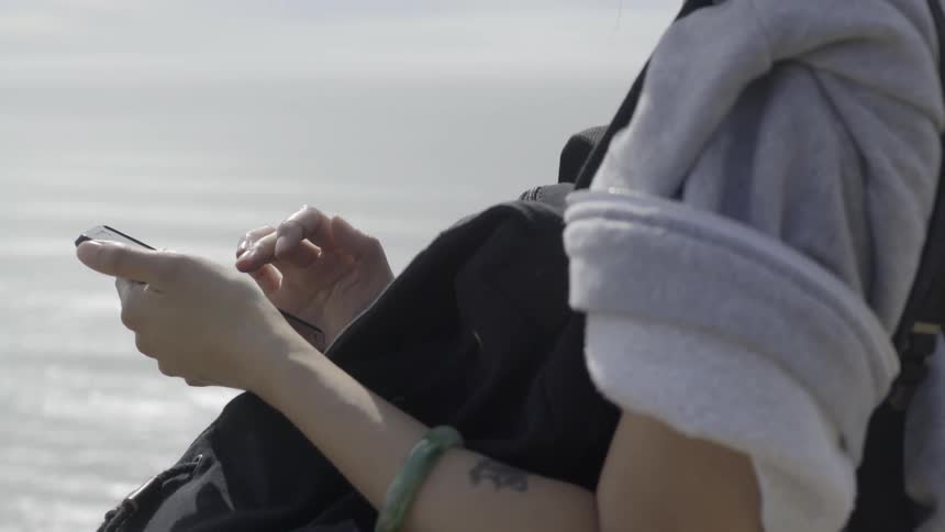 A woman standing near a shore and using a cell phone