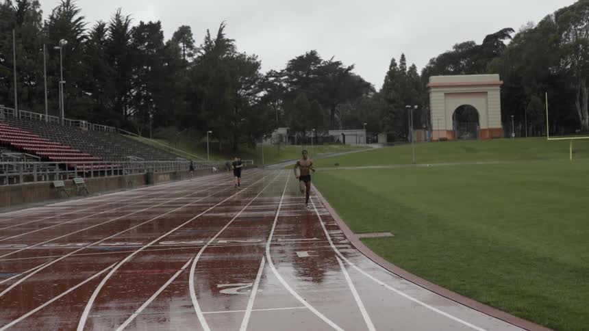 People running on wet outdoor track in heavy rain with gritty energy.