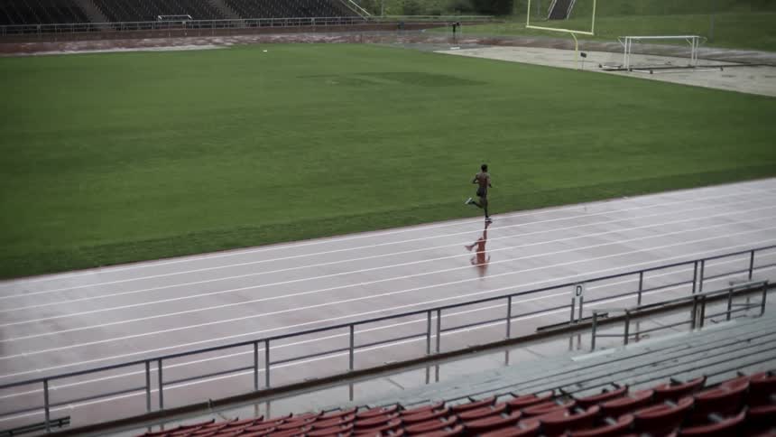 A man running the track at a track stadium on a rainy day