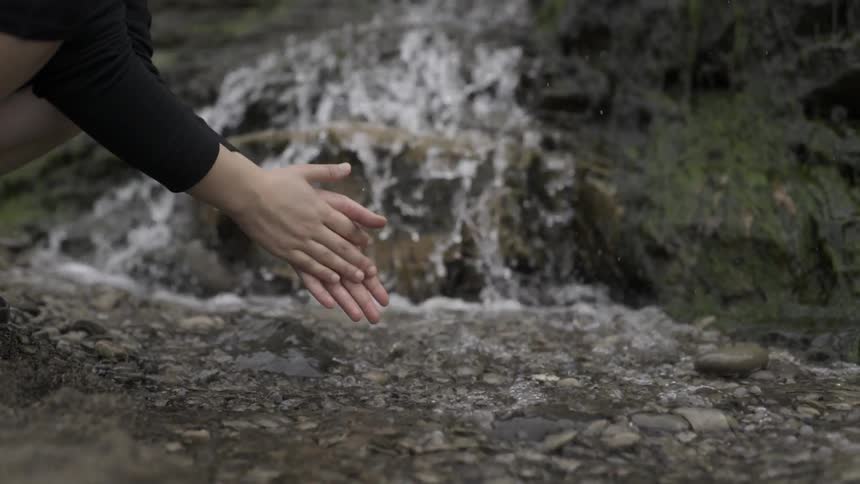 Woman gently rinsing her hands in flowing stream with mindful peaceful stillness.
