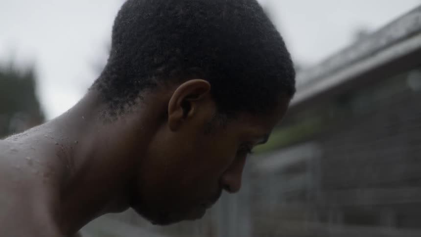 Man standing in rain looking down with quiet introspective emotional mood.