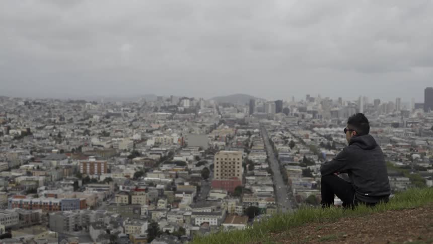 Man sitting on hill overlooking city skyline with thoughtful reflective mood.