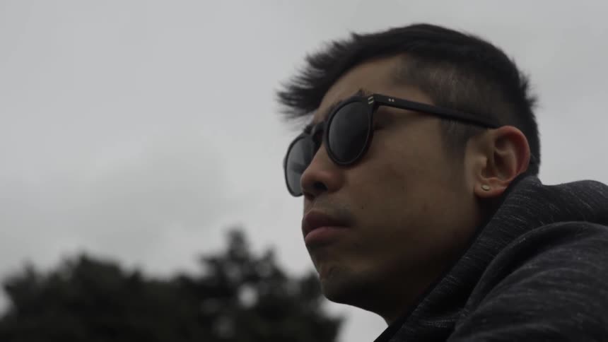 A man wearing sunglasses looks pensively into the distance