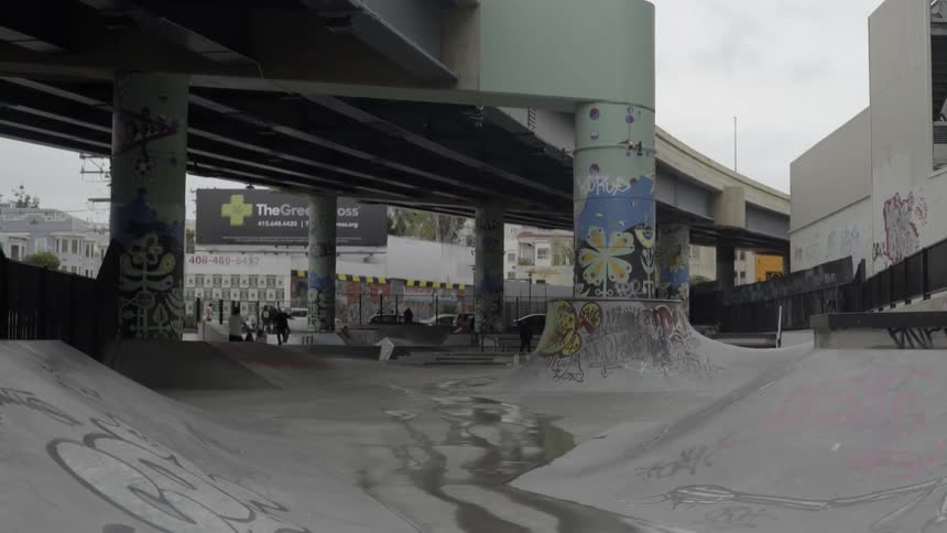 Someone skateboarding under an overpass as others walk along the street