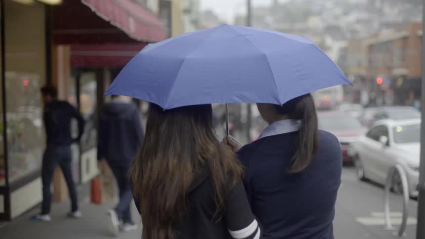 Several people walking down a city street in the rain with two of them sharing one umbrella