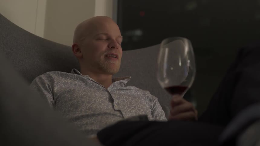 Man sitting in chair holding wine glass and talking with relaxed confidence.