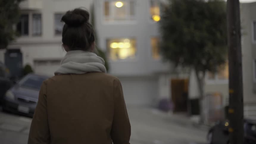 Woman in brown coat walking down city street with calm reflective pace.