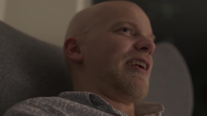 Man sitting in chair talking to someone off-camera with engaged relaxed vibe.