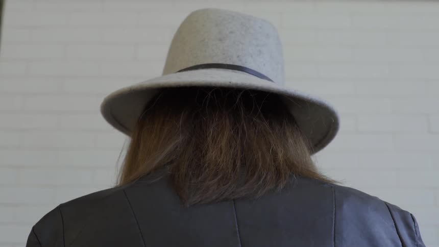 A woman wearing a hat is seen from behind as she turns her head