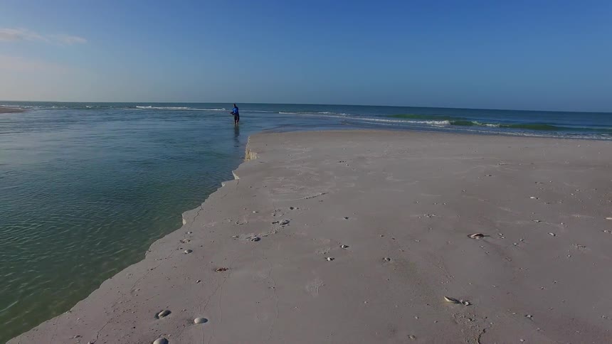 A man wading along a beach and reeling something in