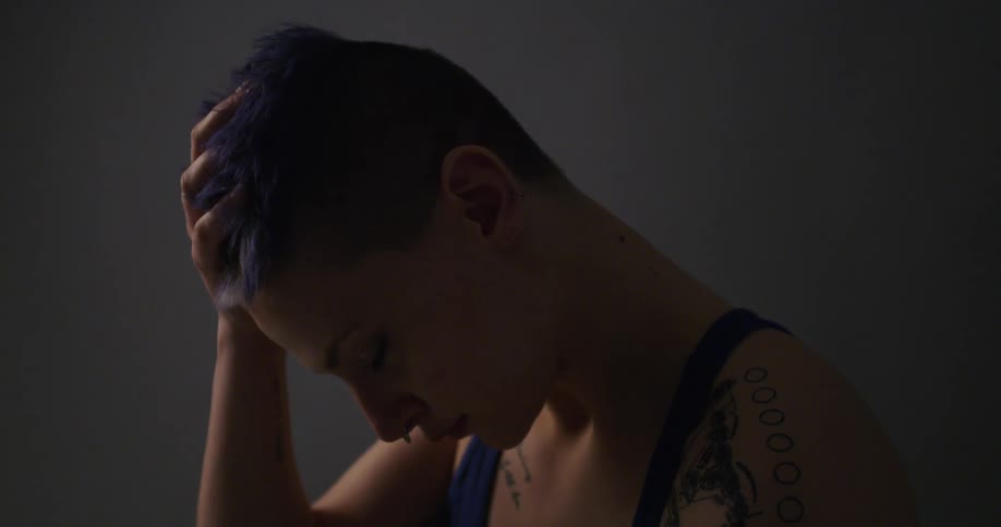 A young woman looks down and rubs her hand through her hair