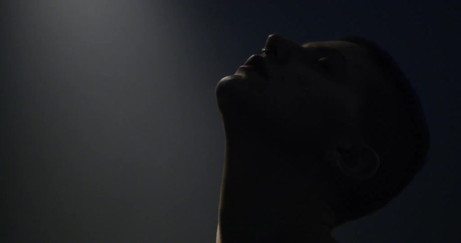 Woman leans her head back looking toward the ceiling in shadowy room