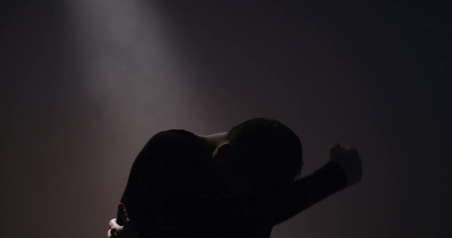 Silhouetted man with arm on head leans to side and embraces himself