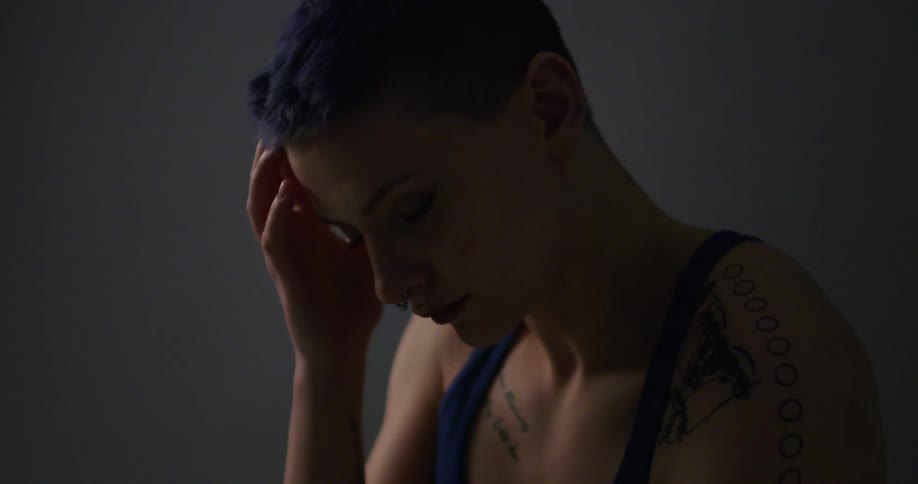 A woman with blue hair and tattoos runs her hand through her hair