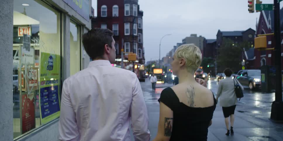 A man and woman walk down a city street holding hands