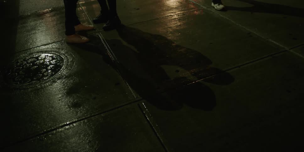 Couple standing on sidewalk at night project shadows on the wet concrete