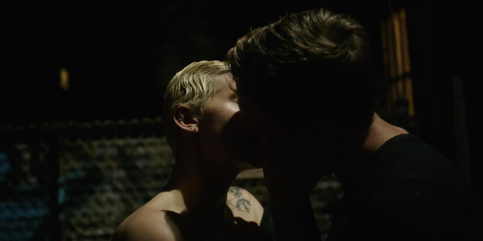 A white woman and white man kiss while standing outdoors at night