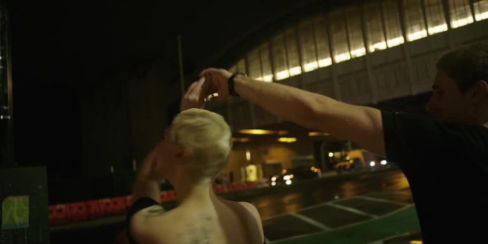 A man and woman dance on a sidewalk at night as road traffic passes by