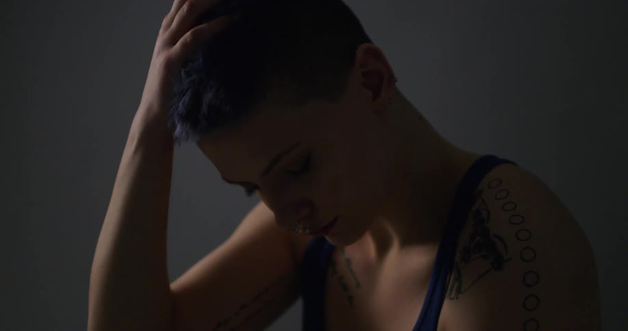 A woman sits looking down with her hand on her head