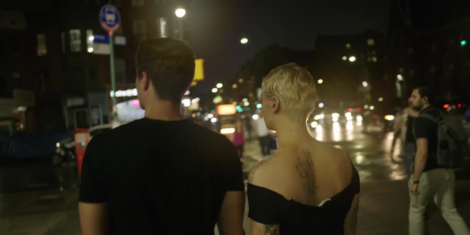 Young couple holding hands walking down city sidewalk at night