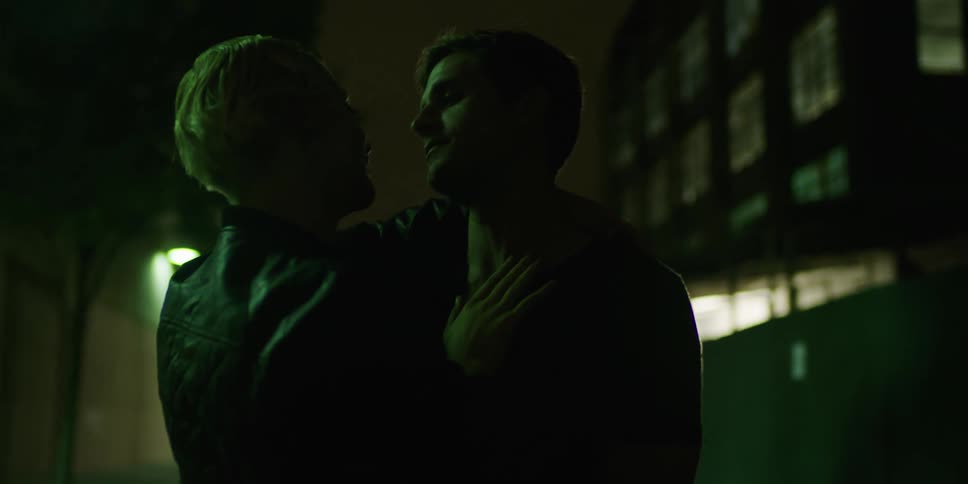 Couple stand and touch each other at night near apartment building