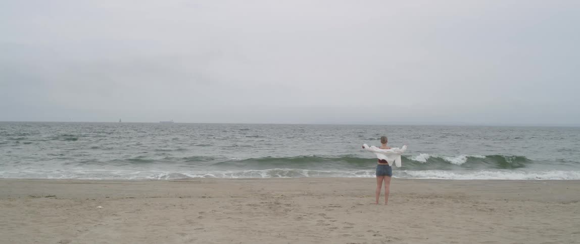 Woman walks on empty beach under overcast grey sky