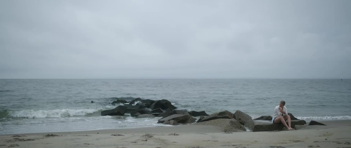 Barefoot woman sitting on a rock in a beach next to the ocean