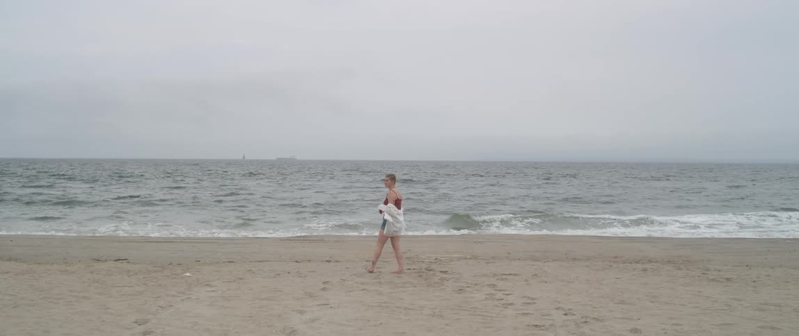 Barefoot woman walks on sand beach next to the ocean on cloudy day