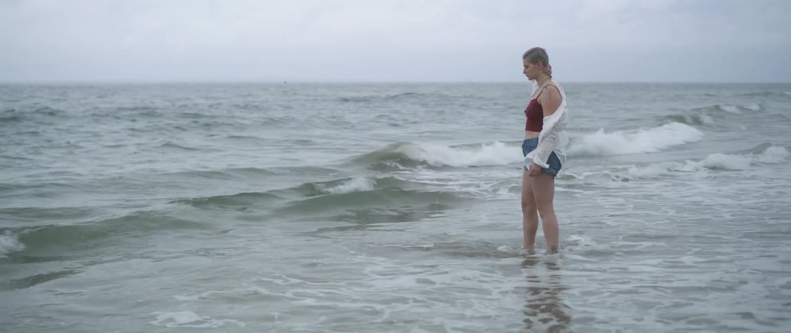 Waves lap the feet of a woman walking along the beach