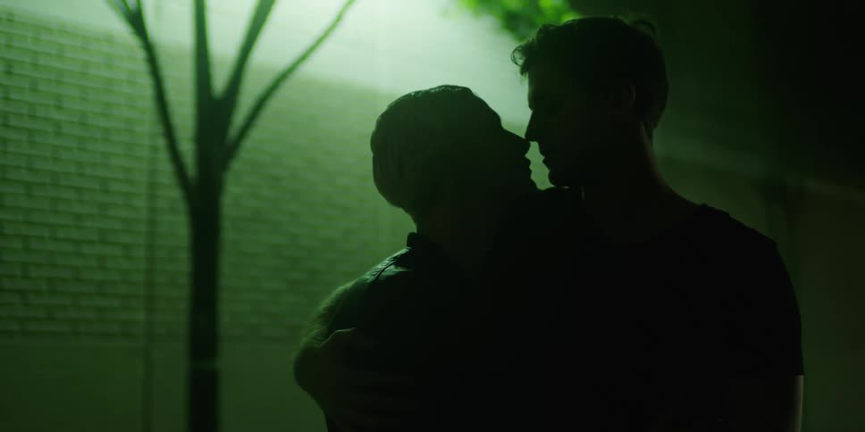 A man and woman embrace and kiss in the dark