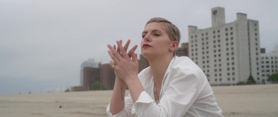 Woman sits on beach in front of hotel under grey sky