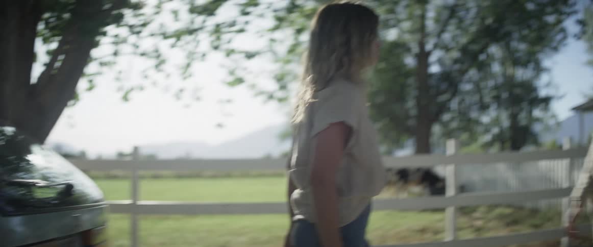 Daughter hugs mother near pasture fence after putting suitcase in car
