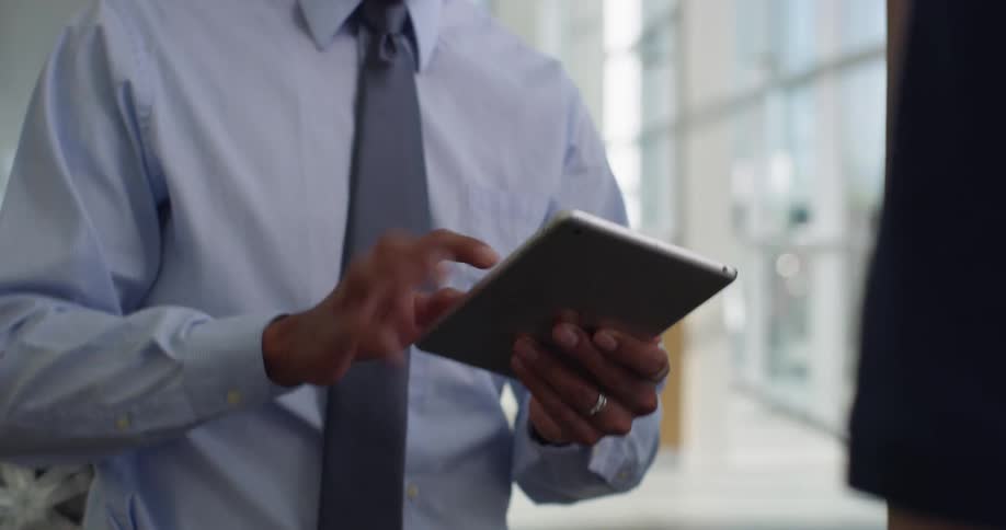 A man hands a tablet to a man with a shirt and tie he uses his finger to sign his name hands it back and shakes hands