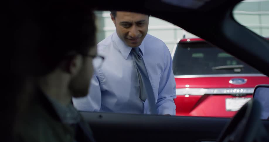 Two people are in a car and a man at the car rental agency hands a key through the window