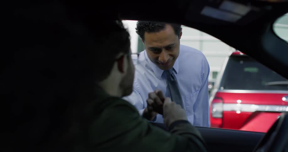 A man and a woman in a car taking keys from another man standing outside with a shirt and tie