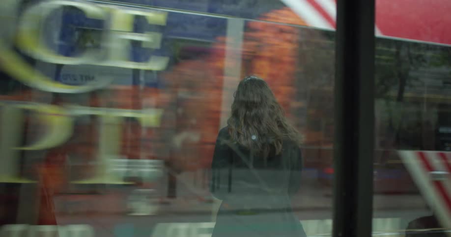 A woman stands inside a bus stop waiting for the city bus