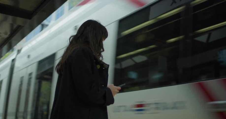 A woman in a coat stands in a train station while using her smartphone