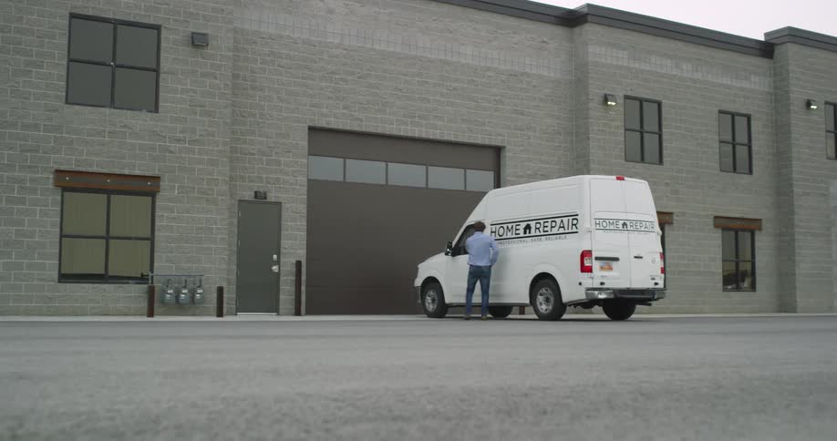A repair man gets into a company van behind a building
