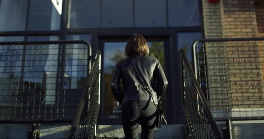 A woman walking upstairs towards a building and tries to open the door with keys