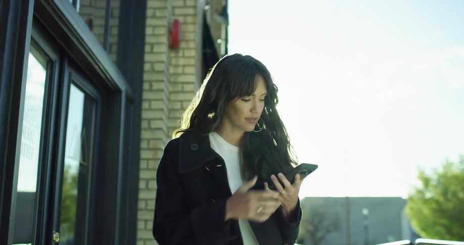 A woman walks out of a store and texts on her cell phone as she walks
