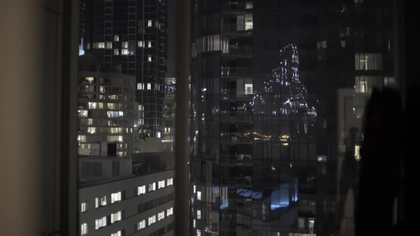 Woman Standing by a Mirror Building Wall Gazing Thoughtfully Out at the City Below.