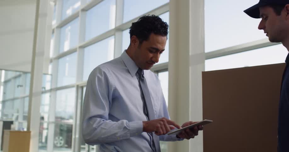 Professional man walking up to delivery man signing for package on a tablet
