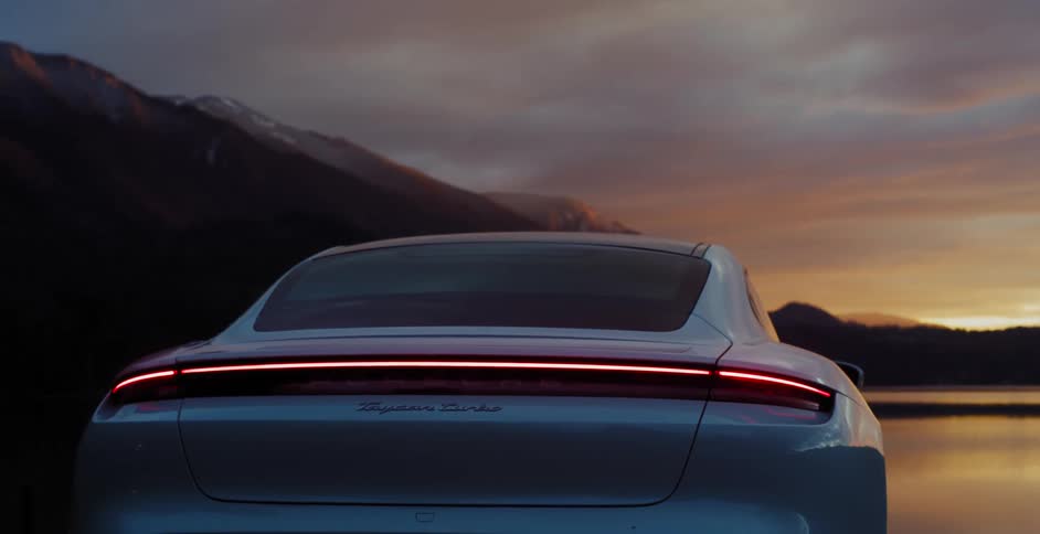 Porsche taycan parked in front of a lake near mountains at sunset