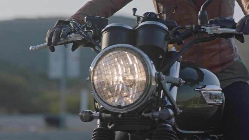 A motorcyclist rides down a road with a lit headlight